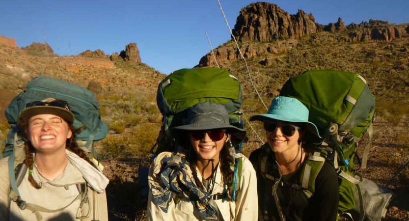 a group of gap year students carrying backpacks smile at the camera while standing in front of a rock formation in texas